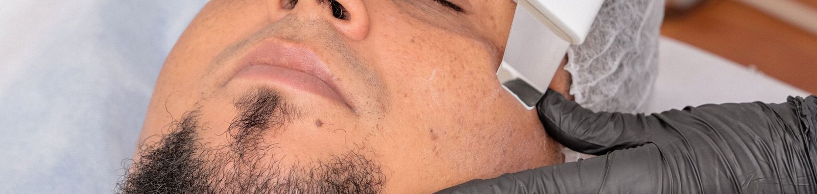 A man undergoing a facial treatment with advanced cosmetology equipment.