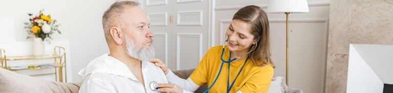 A nurse uses a stethoscope for a home check-up on a senior adult in a cozy living room.