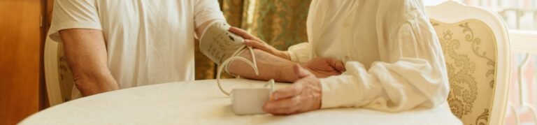 An elderly couple at home measuring blood pressure with a digital monitor, depicting care and health awareness.