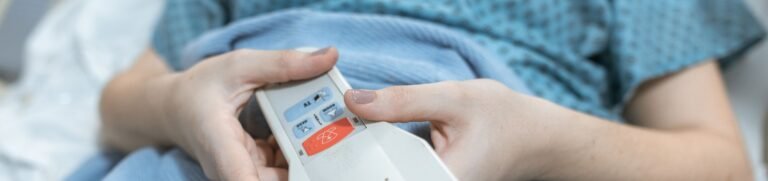 Close-up of a patient's hands holding a remote control in a hospital bed, showing care and medical settings.