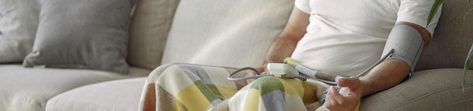 Elderly man monitoring blood pressure on a cozy couch at home, surrounded by medication.