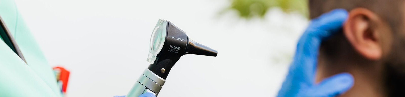 Healthcare professional examining patient's ear with an otoscope in a clinical setting.